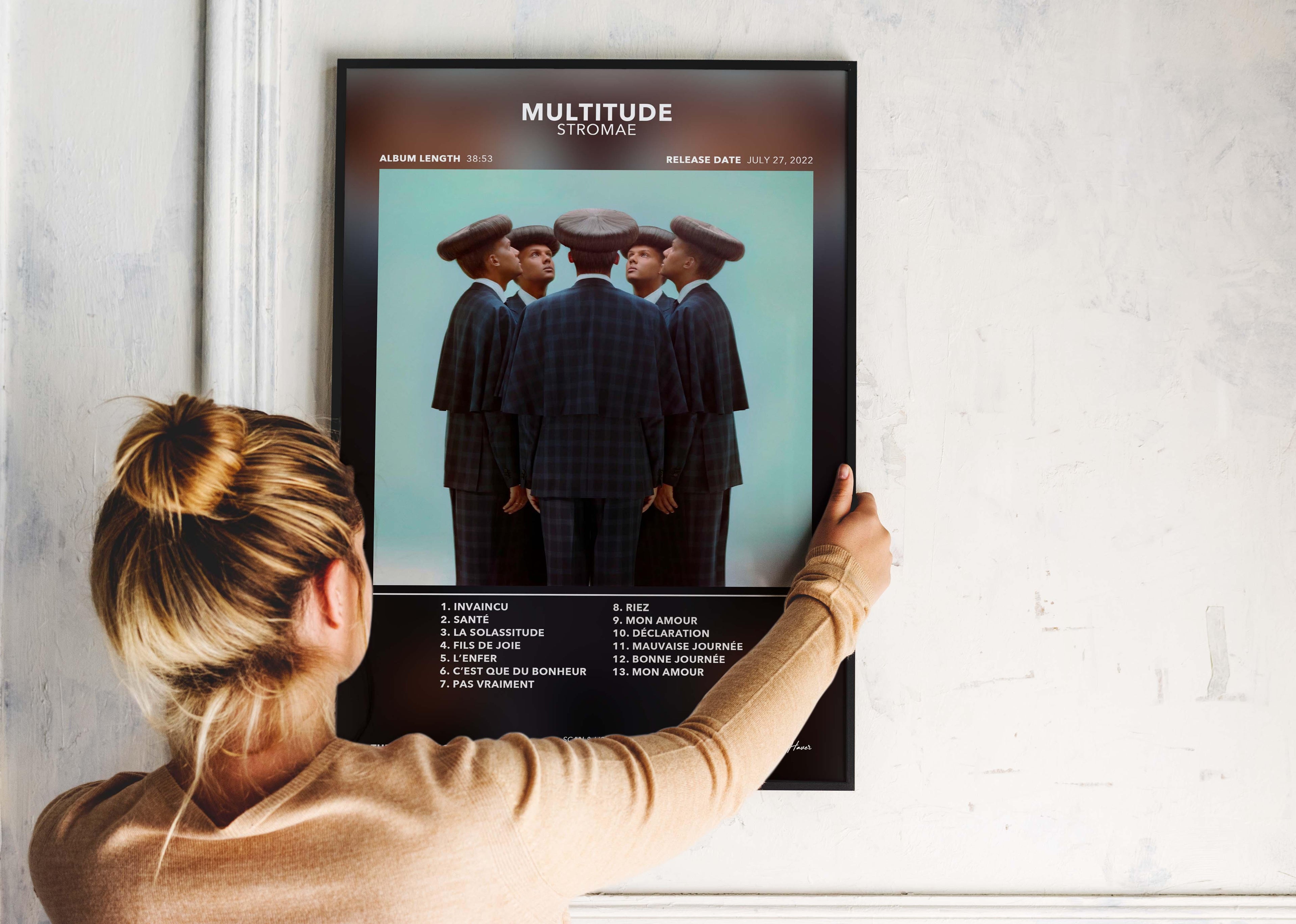 Une femme accroche un cadre photo murale avec pochette album "Multitude" de Stromae, fait en France, livraison gratuite 48h