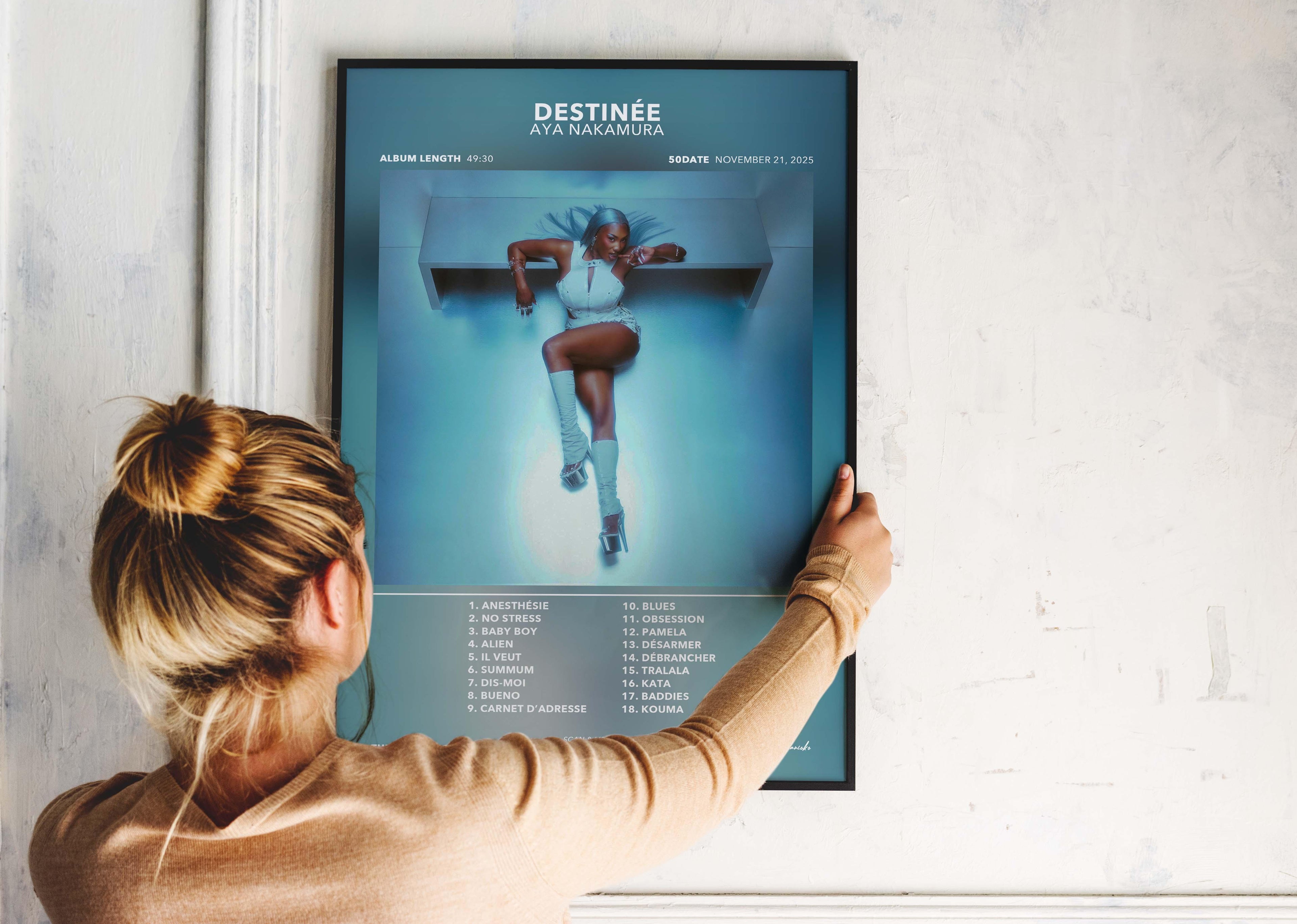 Une femme accroche un poster de l'album Destinée d'Aya Nakamura, fait en France, livraison gratuite 48h