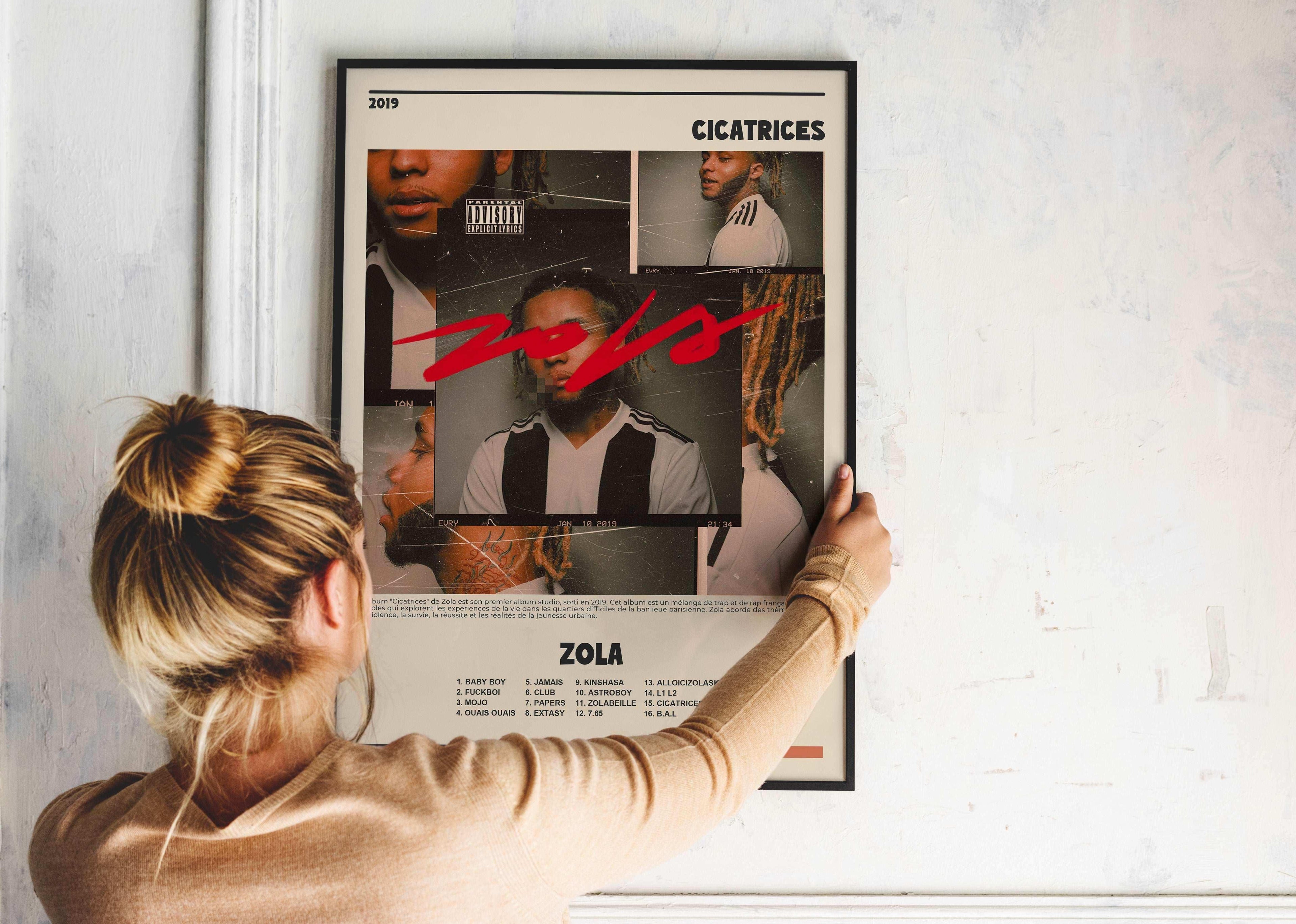 Femme accrochant un poster album Zola Cicatrices sur un mur, fait en France, livraison 48h, cadeau idéal Noël
