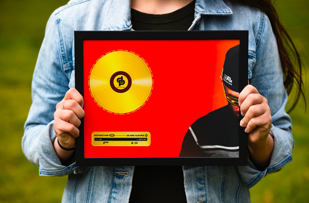 Personne en jean tenant un cadre noir avec disque d'or et texte jaune sur fond rouge, fait en France, livraison gratuite 48h