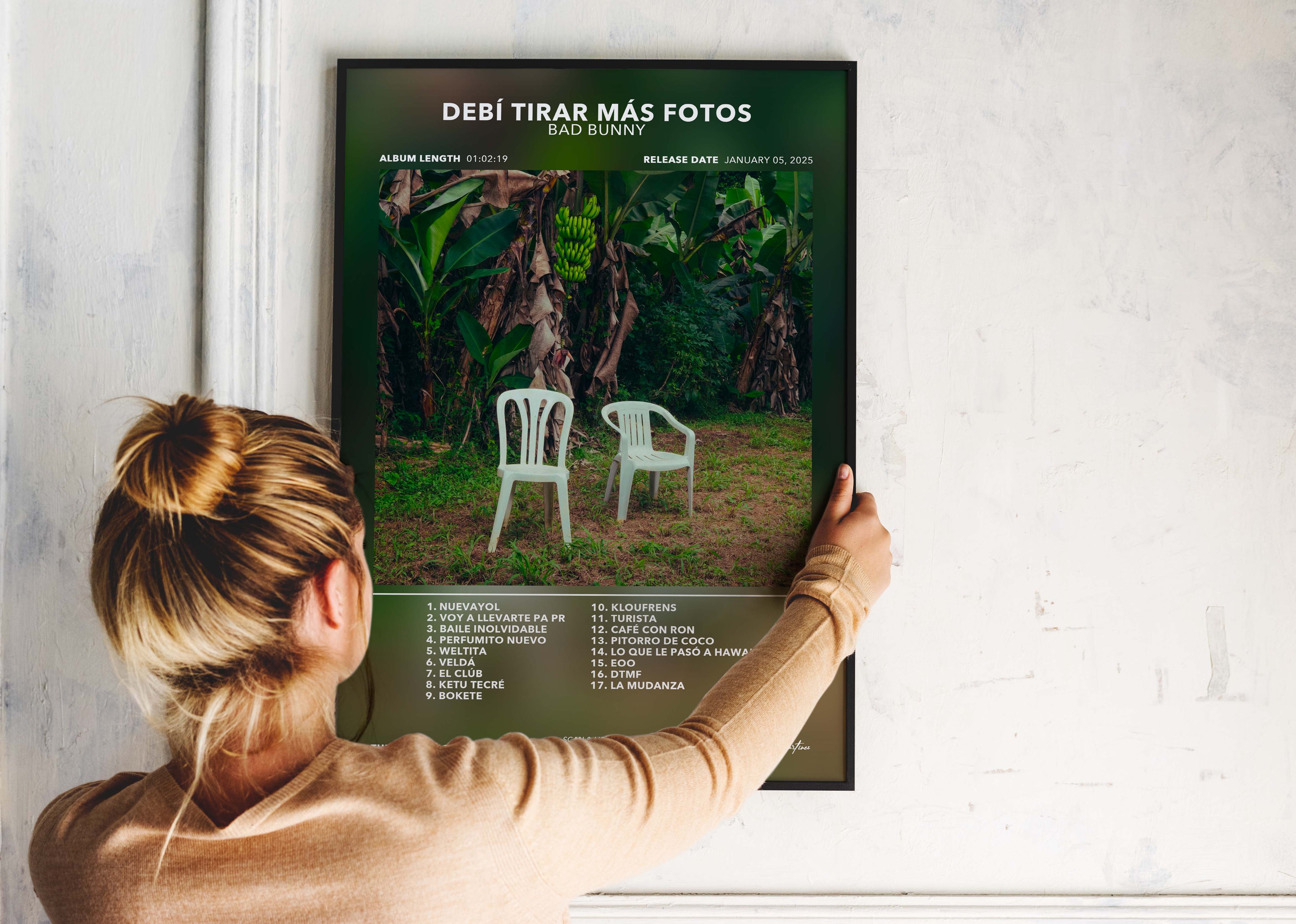 Une personne installe le poster encadré de Bad Bunny Debí Tirar Mas Fotos sur un mur blanc de salon, montrant la mise en valeur de la pièce.
