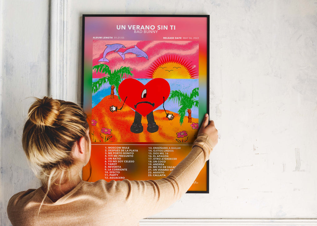 Une personne installe le poster encadré de Bad Bunny Un Verano Sin Ti sur un mur blanc pour décorer son espace personnel.