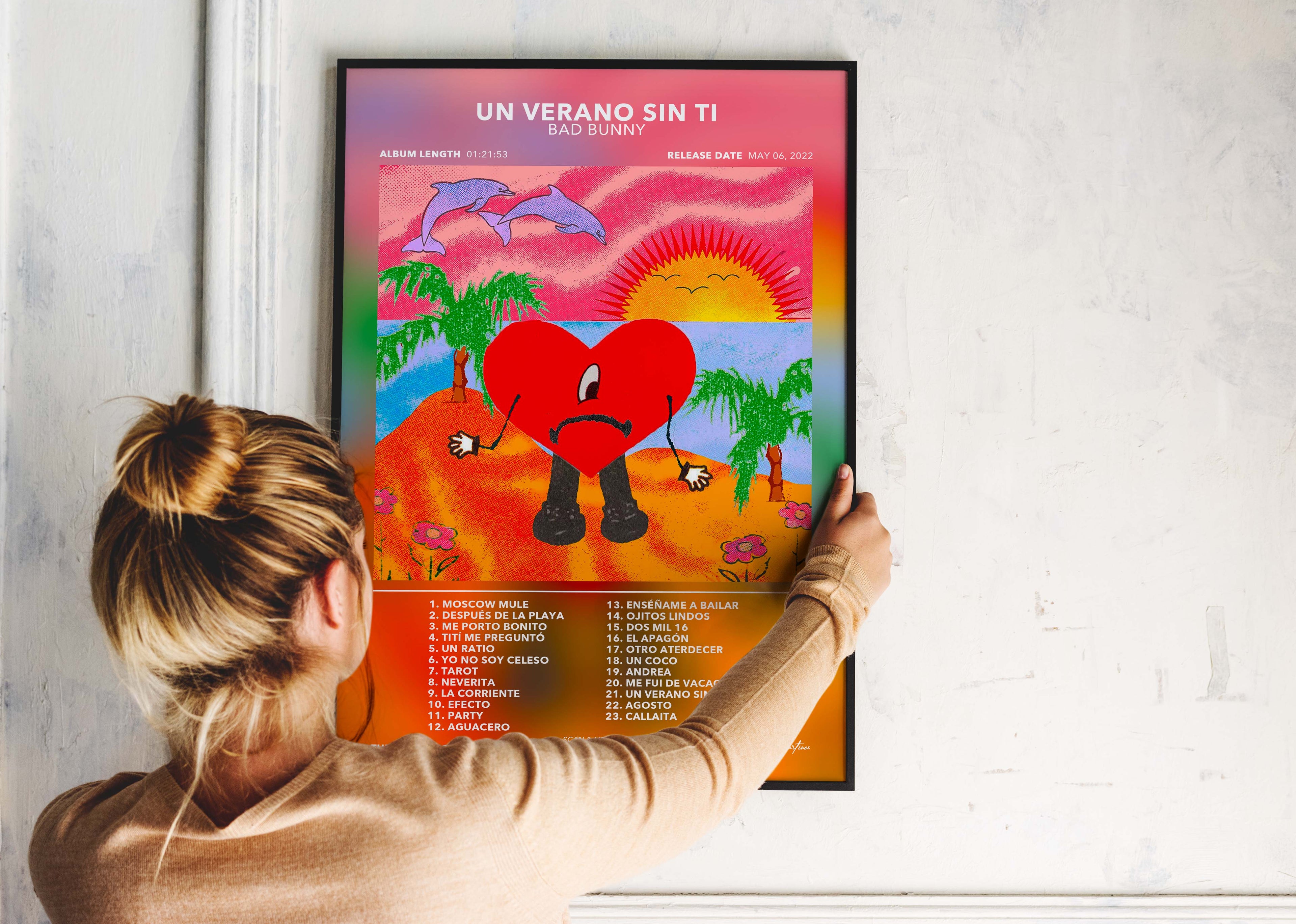 Une personne installe le poster encadré de Bad Bunny Un Verano Sin Ti sur un mur blanc pour décorer son espace personnel.